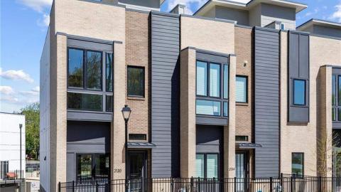 A large brick and glass townhome with a rooftop in the sunlight under blue skies. 