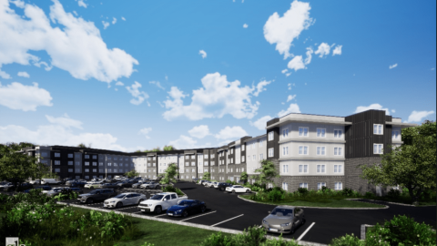 A long low apartment community set on a parking lot under blue skies. 