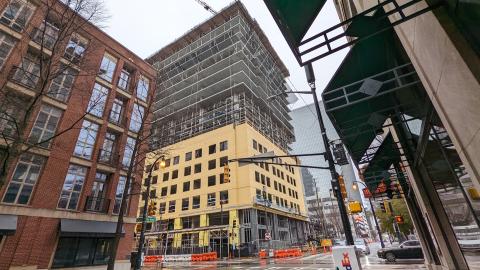 A photo of a tall building being constructed in downtown against gray skies. 