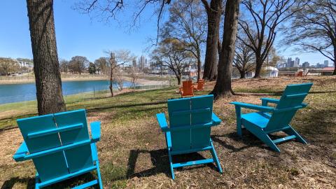 A photo of a park beside a lake with blue and orange chairs and Atlanta's skyline beyond. 