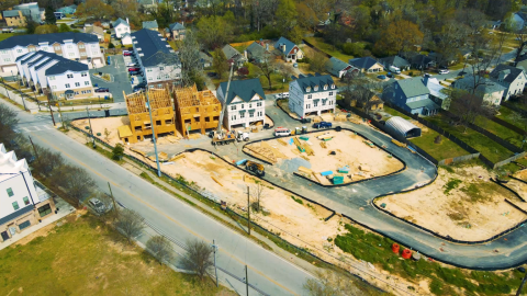 A construction site where many duplexes are being built beside a large road. 
