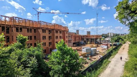 A photo of a large wooden apartment complex being built beside streets and a dirt trail. 