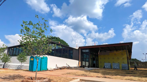 A photo of a black and white long, low building under blue skies and fluffy clouds.