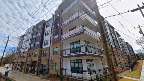 An apartment complex with a stone and red and white plank facade under cloudy skies in Atlanta.