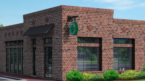 A rendering of a small red brick building under blue skies with bushes in front. 