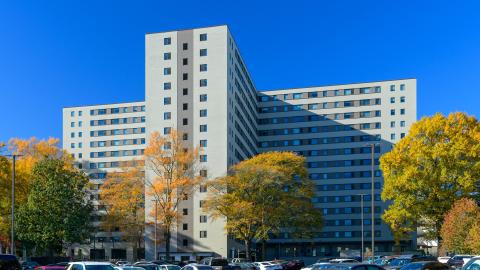 A photo of a white older apartment building under blue skies. 