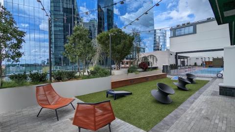 A photo of a large new brick and glass apartment building will a pool and trees as amenities and furnished apartment units.
