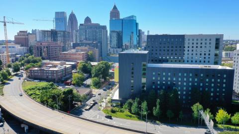A drone photo under blue autumn skies of a black and gray student housing complex near a wide city street. 