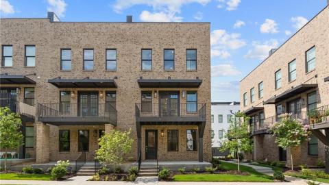 A photo of rows of townhomes with white interiors and green grass in front under blue skies in Atlanta. 