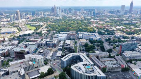 A drone photo over the blocks of West Midtown under blue skies in Atlanta, near many trees.