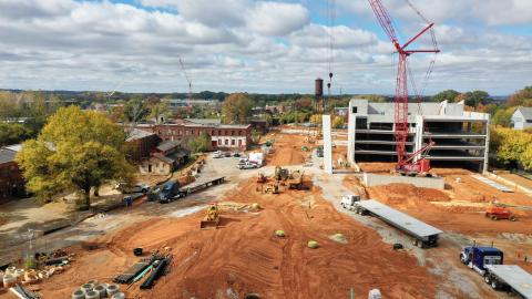 A drone photo of a huge construction site with many old buildings and a new garage and a city skyline in the distance. 