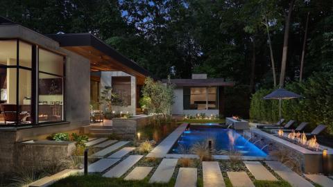 A modern house in white brown and wood exterior with a glass-heavy interior and a pool in the back. 