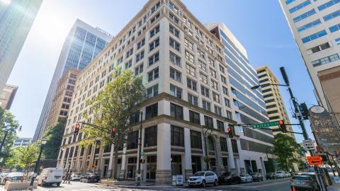 A photo of an old white building under blue skies in downtown Atlanta near many large buildings. 