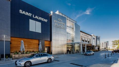 A fancy front of a renovated shopping mall under blue skies with cars in front. 
