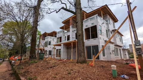 Under gray skies a row of under construction duplexes is being built with many trees in front.