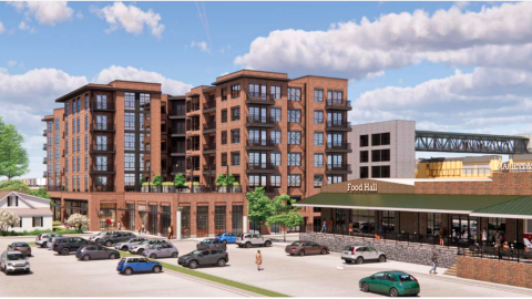 A rendering of a large brick apartment building under blue skies, next to a large market.