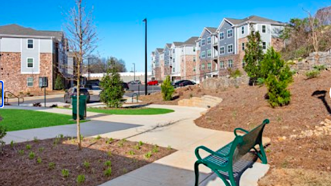 A photo of  large new blue and brick apartment complex with wide sidewalks under blue skies. 