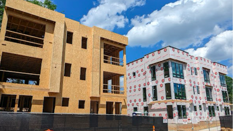 A photo of a large site where townhome are being built under blue skies near large roads. 