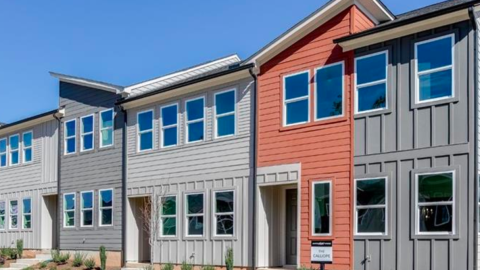 A gray and blue and orange townhome project under blue skies on a field in Atlanta, next to a large greenspace.