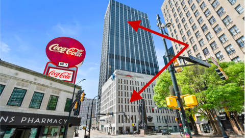 A photo with two red arrows showing a tall black building and a shorter white one in downtown Atlanta under blue skies. 
