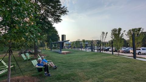 A photo of a large grassy area surrounded by warehouse buildings turned into retail spaces and restaurants.