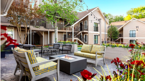 A renovated apartment complex shown with flowers and many chairs outdoors under blue skies. 