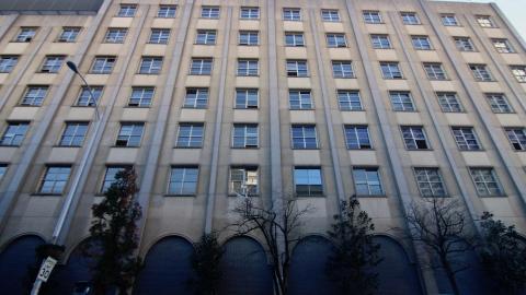 A photo of a large gray building made of concrete with many old windows. 
