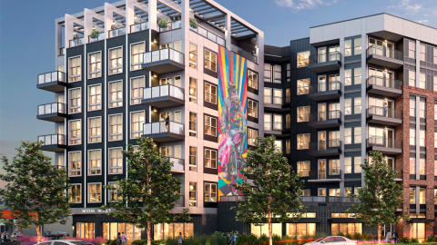 An image showing a brick and glass mid-rise development site under blue skies on two wide streets.