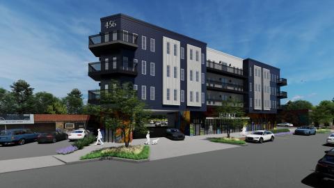 An image of  a large blue and gray apartment building over retail space with a wide street in front.