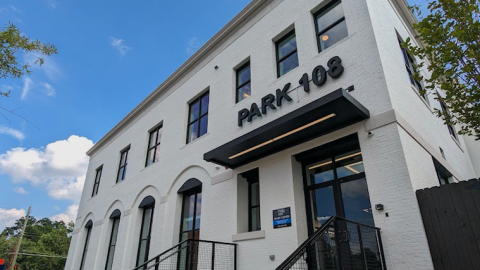 A white older three-story brick building under blue skies with modern-style condos inside. 