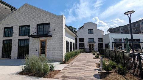 An image of a large apartment complex with a pool and coffee shop under blue skies next to a wide walking path.