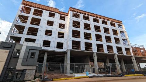 A photo of a large development site with a five-story building and a huge construction zone under blue skies.