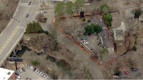 An image of garden style apartments where with many tall trees near a wide road and creek in Atlanta.