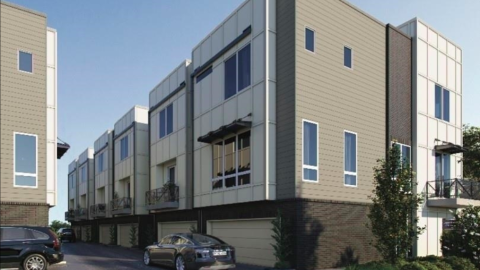 An image of a new brown white and beige townhome under blue skies near a wide street.