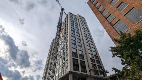 A new gray tower with many windows shown under gray skies next to a massive brick building in Atlanta.