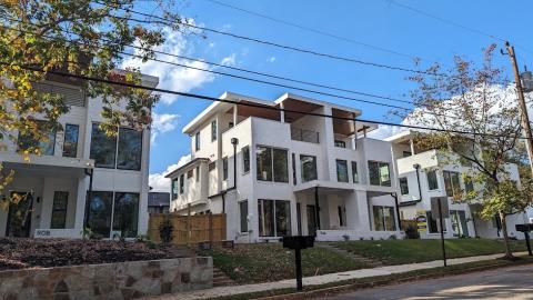 A photo of rows of large duplex houses under blue skies near a wide street with small trees in front. 