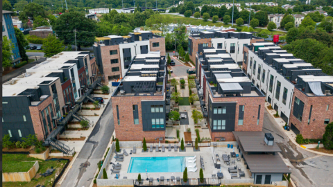 An image showing a row of modern townhomes with brick and white and gray siding near a wide road.