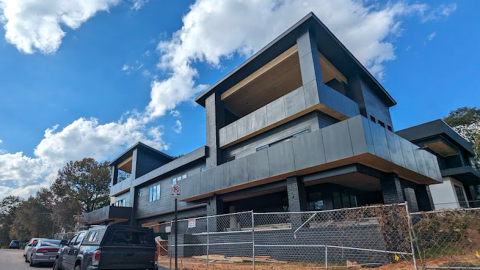 A photo of a large black duplex under blue skies near a wide street and many cars in Atlanta.