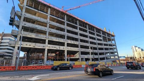 A photo of a large concrete structure under blue skies with cranes above it near a wide street in Atlanta.