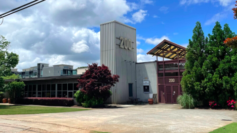 A site with a large 1950s office building on a wide street with a large parking lot behind it. 