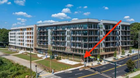An image of a new apartment building with retail at the bottom along a gravel trail where a multiuse path is being built. 