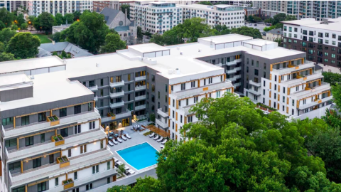 A photo of a white and gray condo building in Midtown Atlanta with white interoirs and a pool near many tall buildings. 
