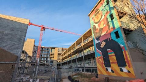 A photo of a large concrete apartment stack under blue skies under construction near a wide pedestrian path.