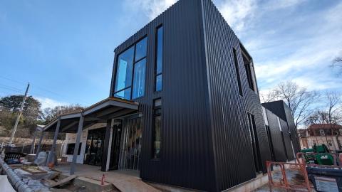 A photo of a large black building under blue skies with large glass windows in front and a wavy roofline.