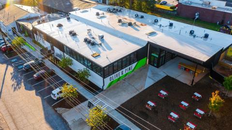 A large white green and black warehouse space remade into a food hall near many trees and picnic tables near Atlanta. 