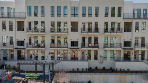 A photo of a large new white condo building under sunny skies with modern stacked homes inside. 