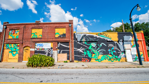 An image of a street with many empty buildings and much graffiti under blue skies. 
