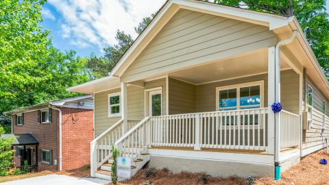 A new house with light-colored siding shown amongst trees on a quiet street in Westside Atlanta.
