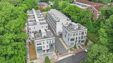 A photo of a white-painted condo and townhome enclave in Atlanta surrounded by many trees and houses under blue skies. 