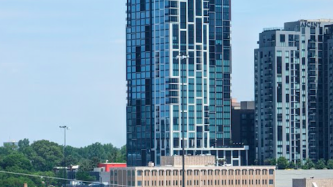 A white and black glassy tower of apartments shown against a blue sky in Atlanta's skyline. 